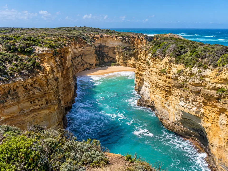 A narrow sea gorge between tall honey-coloured cliffs with a small sandy beach