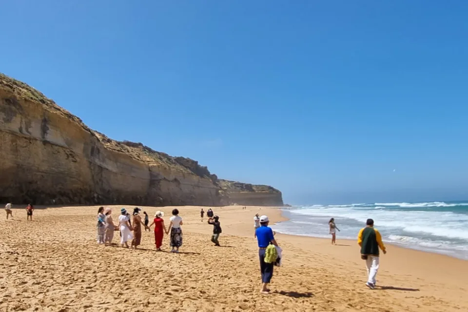 Walkers on the wide beach below tall limestone cliffs at the foot of Gibson Steps